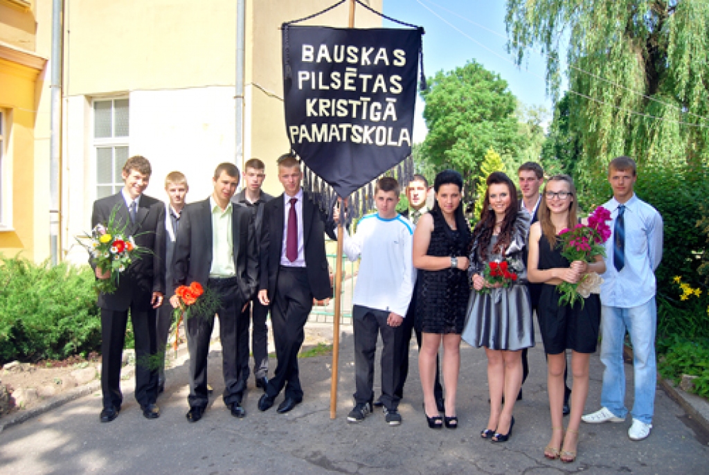 Pie Kristīgās pamatskolas brīdi pirms apliecību saņemšanas piestājuši tās pēdējie absolventi. Viņi nes mācību iestādes karogu.  
Autors: Nikolajs Ševirjovs